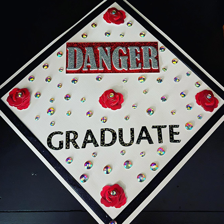 Mortarboard decorated with red flowers and gemstones and says Danger Graduate.