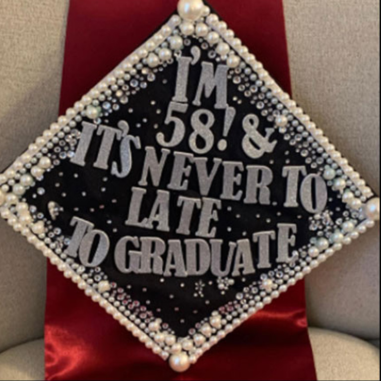 A pearl-encrusted mortarboard reading " I'm fifty-eight! It's never too late to graduate"