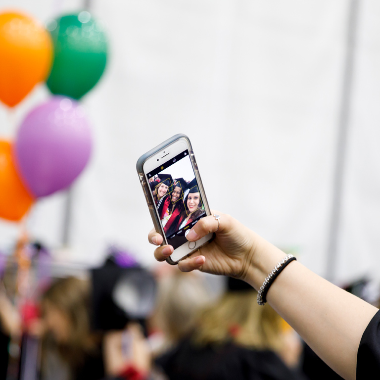 A close-up of a cell phone with three young female graduates in frame